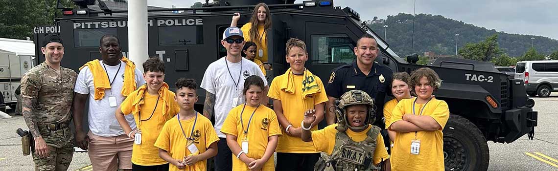 Children posing with SWAT officer with SWAT vehicle in background.