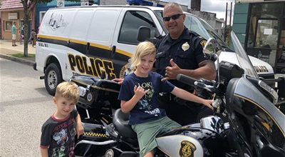 Child sitting on motorcycle unit with officer standing beside him.